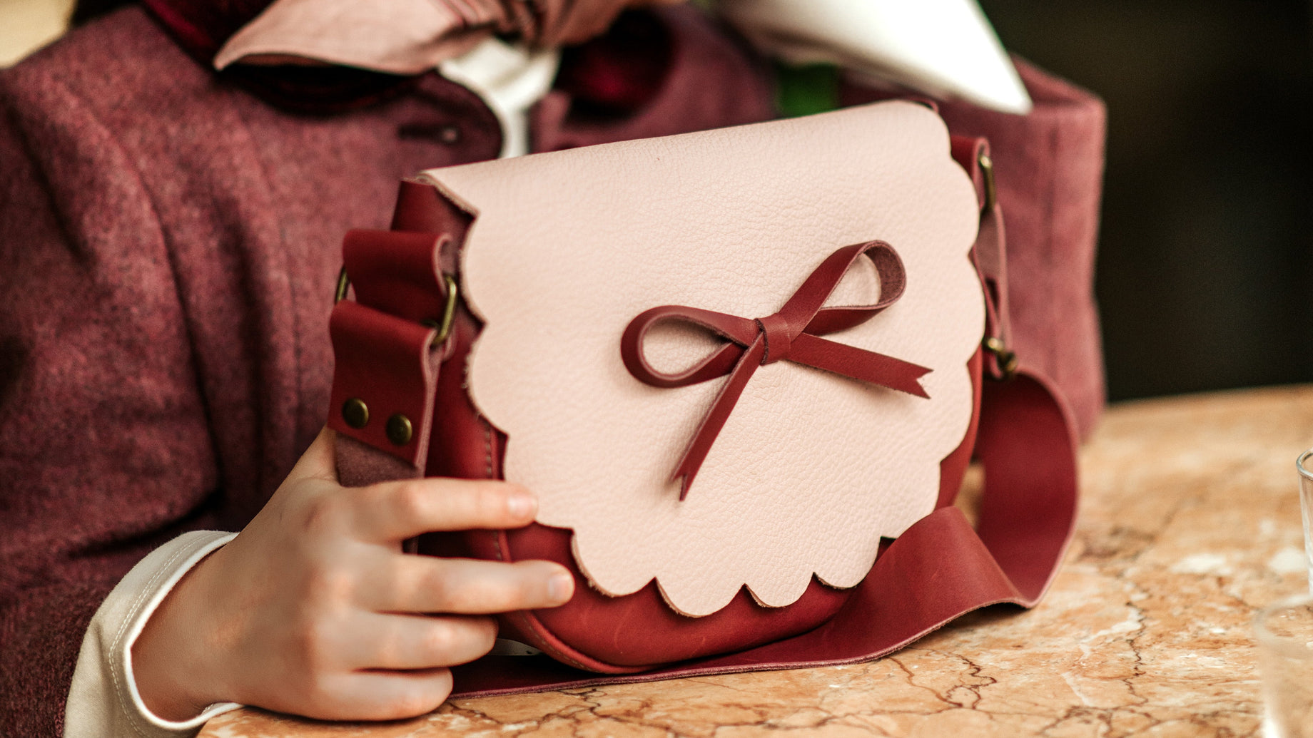 Person holding a pink handbag with a bow, wearing a matching headscarf, on a marble surface with 'L LARK' branding.